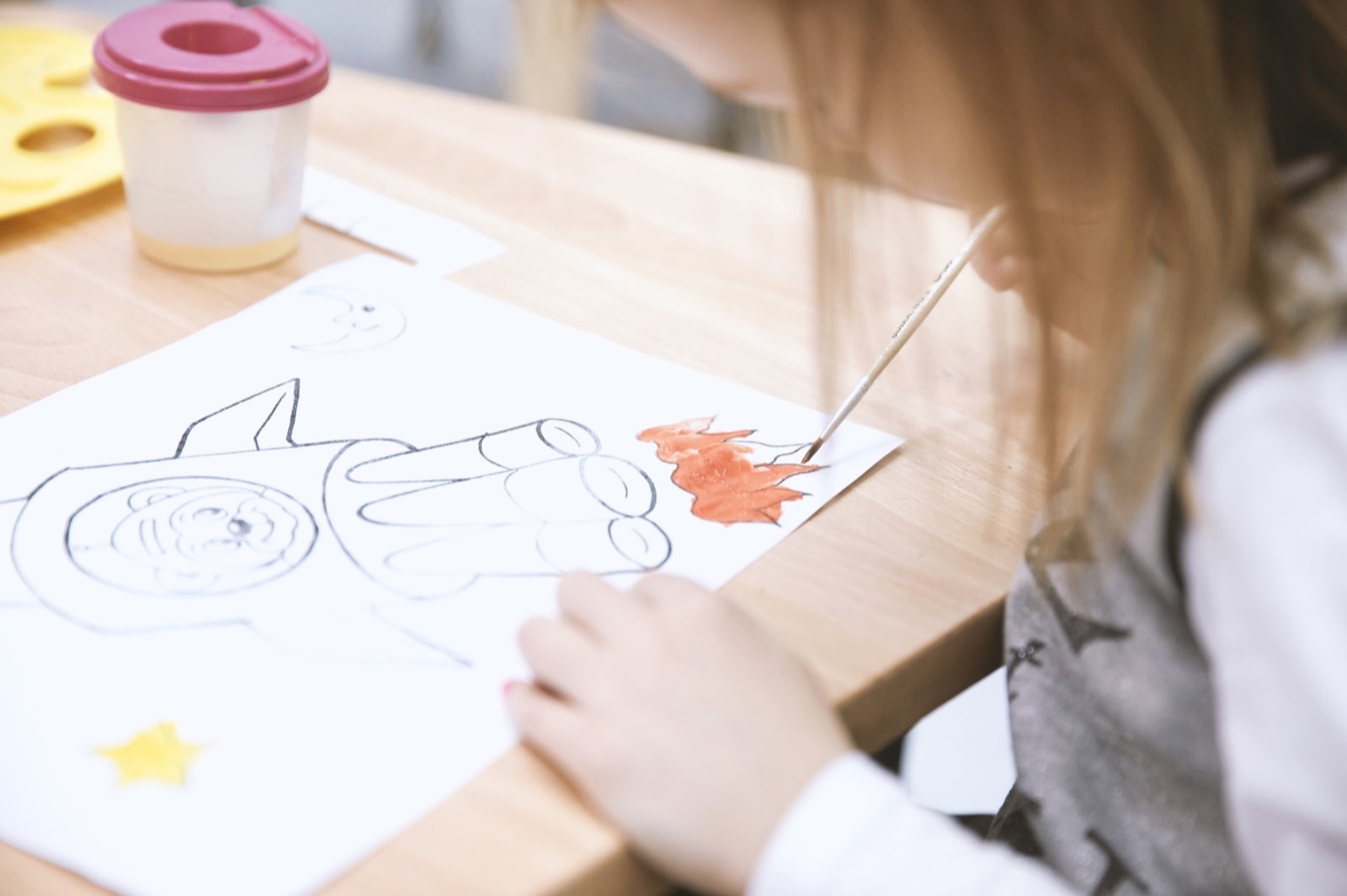 Un enfant dessine et peint sur une feuille posée sur une table en bois