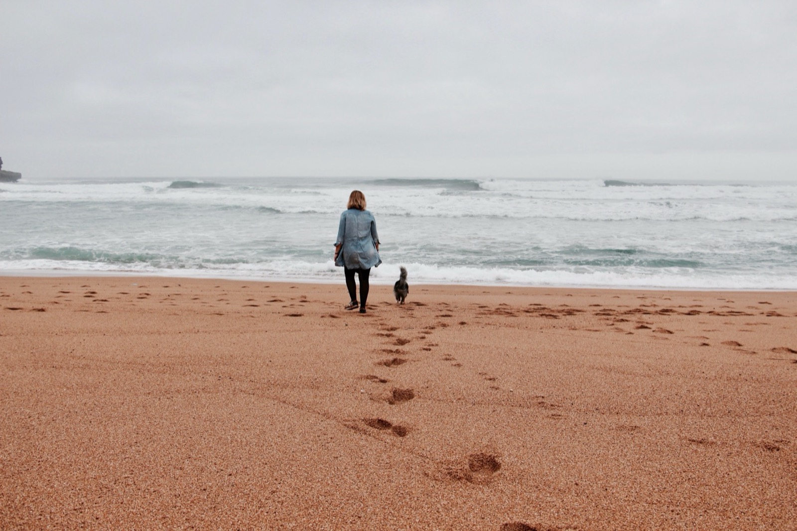 Mary et sa chienne Pyla marchent vers l'océan sur une plage déserte